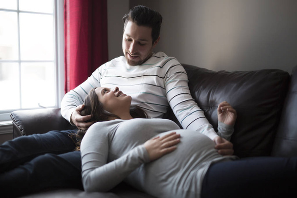 Mid-adult woman expecting baby lying on sofa - Fotoğraf, Görsel