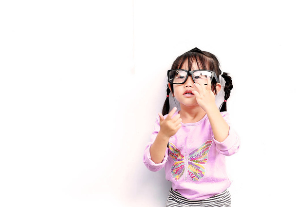 Portrait of cute little girl trying to wear glasses on white background - 写真・画像