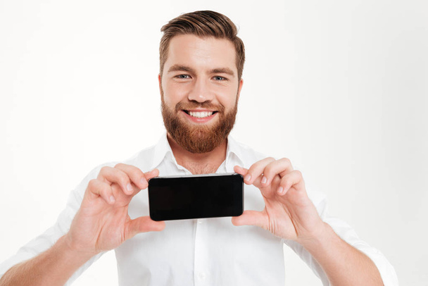 Cheerful young bearded emotional man showing display of phone. - Fotó, kép