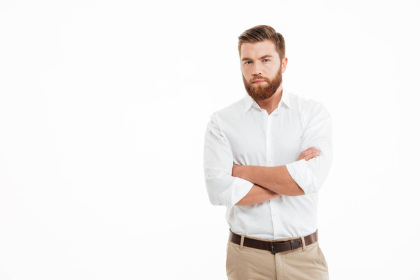 Serious young bearded man standing over white wall - Fotoğraf, Görsel