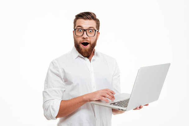 Shocked young bearded man using laptop. - 写真・画像
