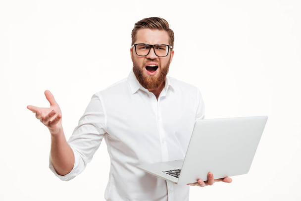 Frustrated man in eyeglasses holding laptop and gesturing with hand - Fotoğraf, Görsel