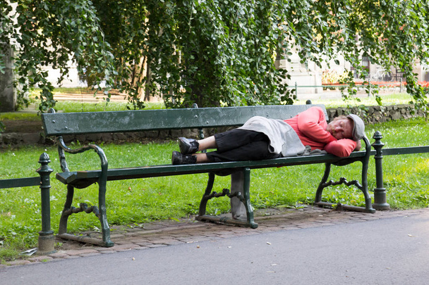 POLONIA, KRAKOW, Un vagabundo duerme en un banco en el Parque
 - Foto, Imagen