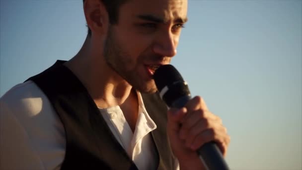 Mladý muž se zpívá na ulici v letním dni, drží mikrofon - Záběry, video