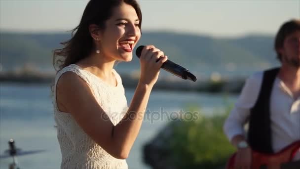 Uma menina jovem e bonita canta uma canção energética em um microfone ao ar livre
 - Filmagem, Vídeo