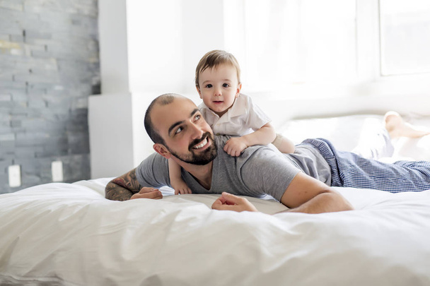 Beautiful man and son lying together on a bed - Foto, Imagen