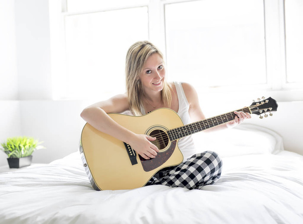 Smiling woman with guitar sitting on the bed - Фото, зображення