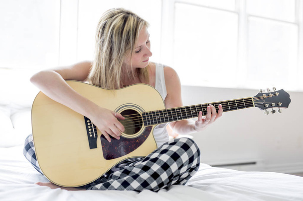 Smiling woman with guitar sitting on the bed - Фото, изображение