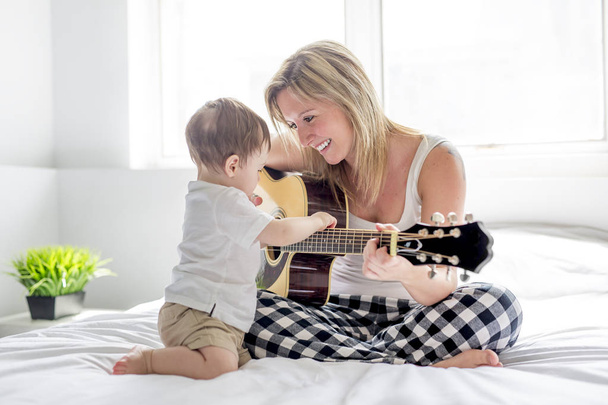 Smiling woman with guitar sitting on the bed with child - Fotó, kép