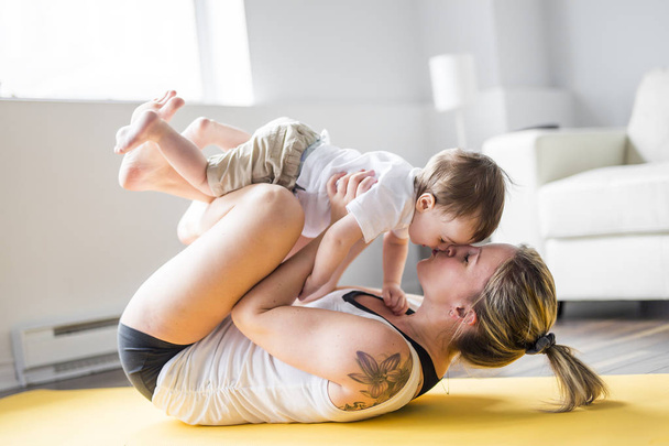 sports mother is engaged in fitness and yoga with a baby at home - Foto, imagen