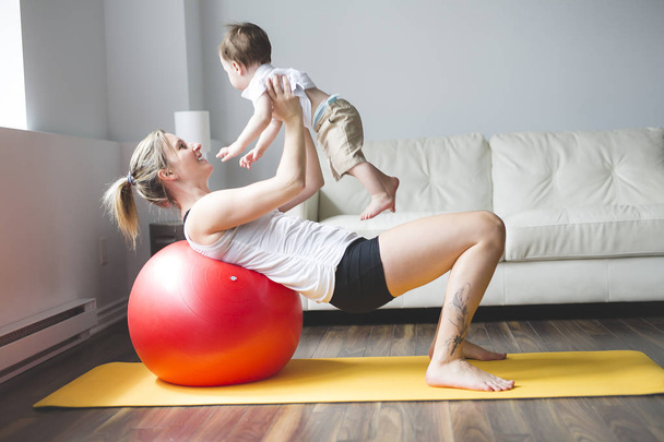 sports mother is engaged in fitness and yoga with a baby at home - Fotó, kép