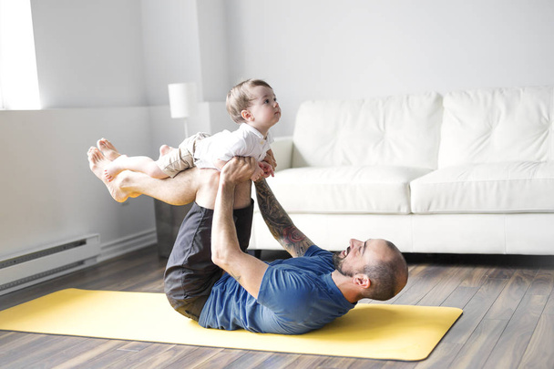 sports man is engaged in fitness and yoga with a baby at home - Φωτογραφία, εικόνα