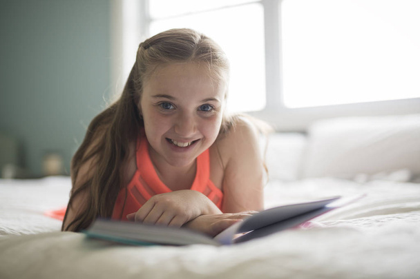 young brunette teen reading a book in bed. - Foto, afbeelding