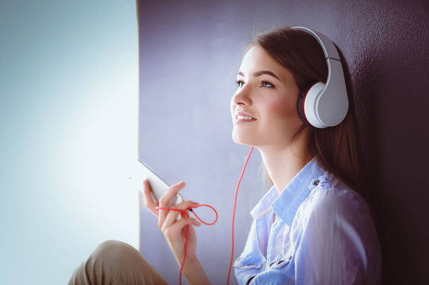 Smiling girl with headphones sitting on the floor near wall - Foto, imagen
