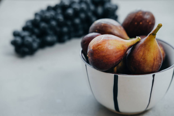 Figs in a bowl and dark grapes on a gray background. Autumn harv - Foto, Bild