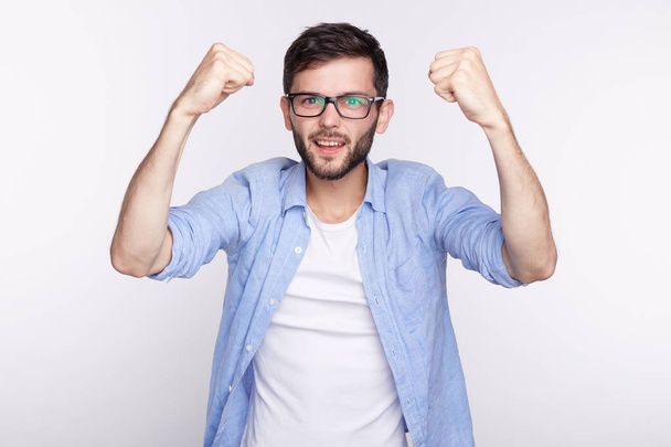 Life perception and achievement concept. Close up shot of happy successful Caucasian student or employee screaming with winning expression, fists pumped, celebrating success against blank studio wall. - Photo, Image