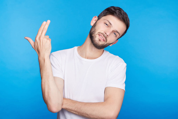 Close up isolated portrait of male Caucasian office manager bored with work, shooting himself with finger gun gesture against blank blue wall background. Human face expressions and emotions concept. - Photo, Image