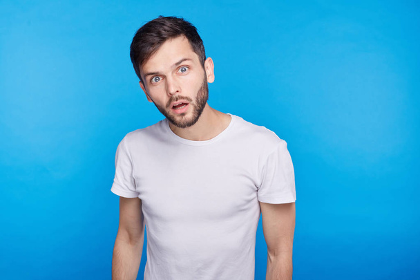 Young man looking with terror into camera with fish eye effect holding  isolated over blue background. Attractive guy having despair looking with wide opened eyes and mouth shouting loudly with panic. - Foto, immagini