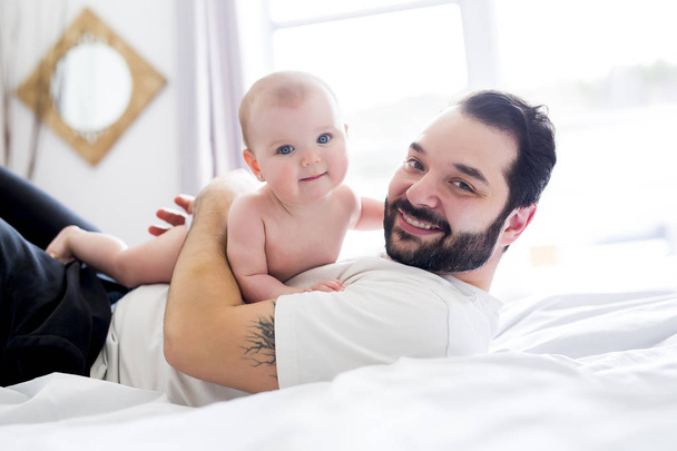 Young happy father playing with babyon bed - Foto, Bild