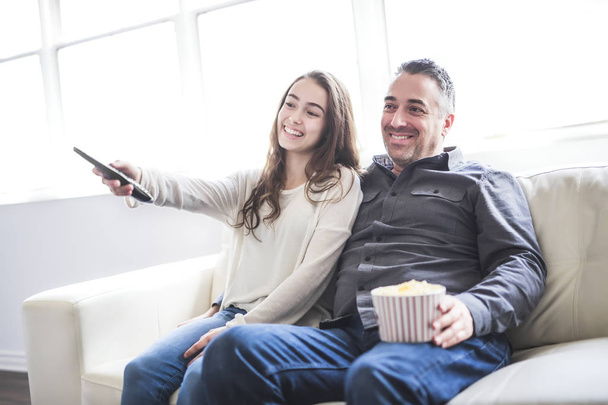 Portrait of a young man and daughter watching TV while eating popcorn on the sofa - Photo, image