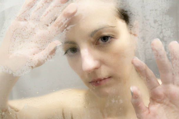 Stressed woman leaning on weeping glass shower door - Foto, imagen