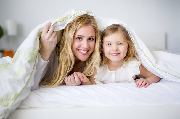 Linda niña y su madre tumbada en una cama
 - Foto, Imagen