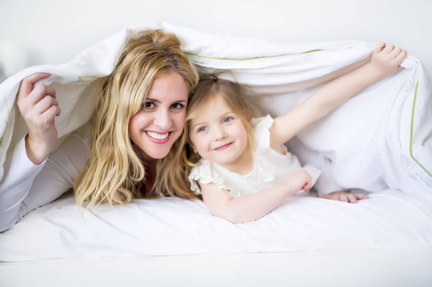 Cute little girl and her mother lying on a bed - Фото, зображення