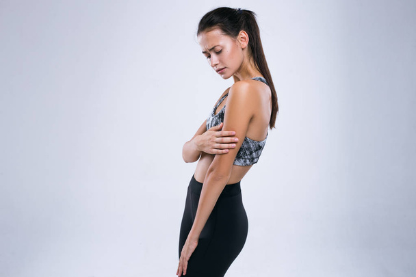 abgeschnittenes Bild einer jungen Fitness-Frau mit Armschmerzen, während sie isoliert vor grauem Hintergrund steht - Foto, Bild