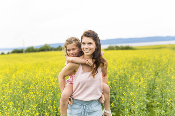 Happy family mother and child daughter embrace on yellow flowers on nature in summer - Valokuva, kuva