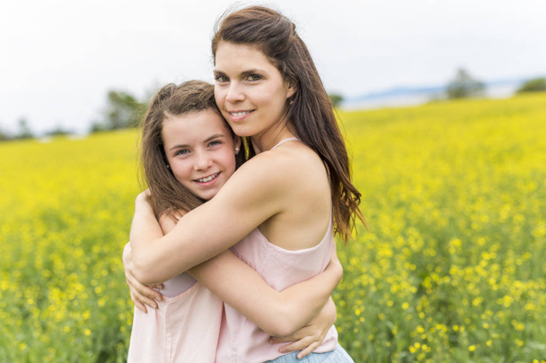 Happy family mother and child daughter embrace on yellow flowers on nature in summer - 写真・画像