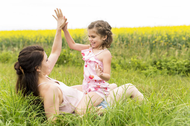 Happy family mother and child daughter embrace on yellow flowers on nature in summer - Фото, изображение