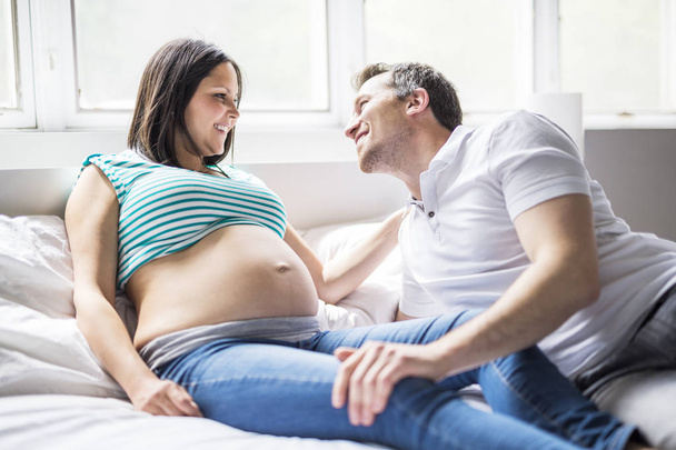 Young parents in bed expecting a little baby, Romantic moments for pregnant couple - Foto, afbeelding