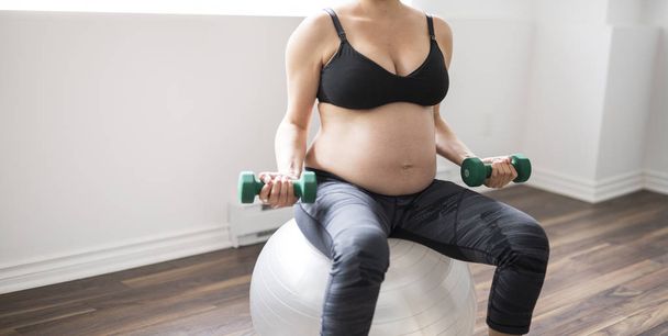 Pregnant woman training with dumbbells to stay active - Photo, Image