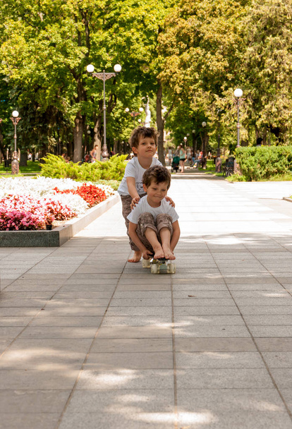 Tweeling jongens rollen elkaar op een skateboard buiten in het park - Foto, afbeelding