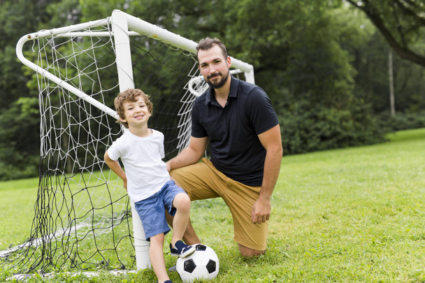 father with son playing football on football pitch - 写真・画像