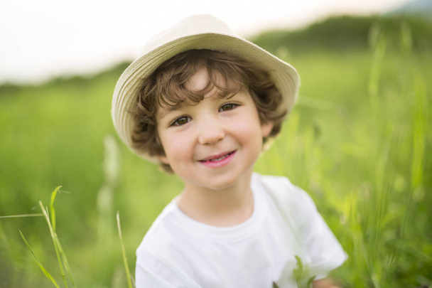 Portrait of adorable kid boy with hat standing on a summer meadow - Fotoğraf, Görsel