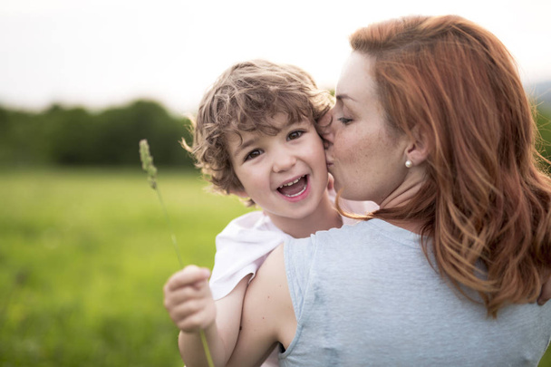 Cute kid boy with his mother on a summer meadow - Фото, изображение