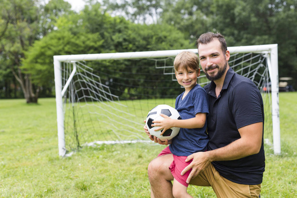 father with son playing football on football pitch - Zdjęcie, obraz