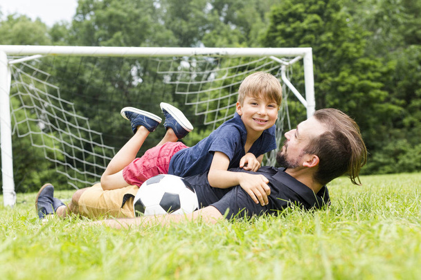 father with son playing football on football pitch - Zdjęcie, obraz
