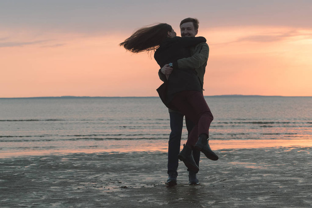 young loving couple is spinning on the seashore in the fall - Foto, imagen