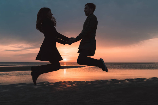 young couple in love jumping at sunset on the beach in autumn - Foto, imagen