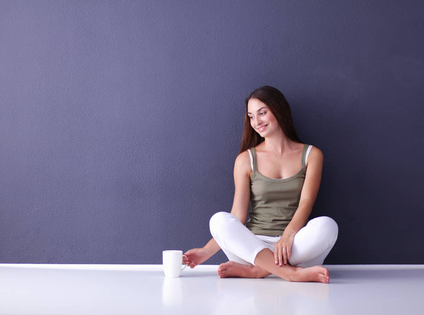 Attractive caucasian girl sitting on floor with cup and tablet near wall - Foto, Imagen