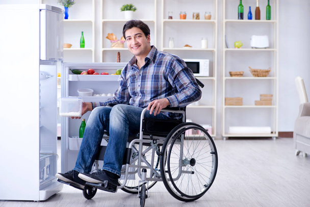 Νεαρός ανάπηρος τραυματίας ανοίγει την πόρτα του ψυγείου - Φωτογραφία, εικόνα