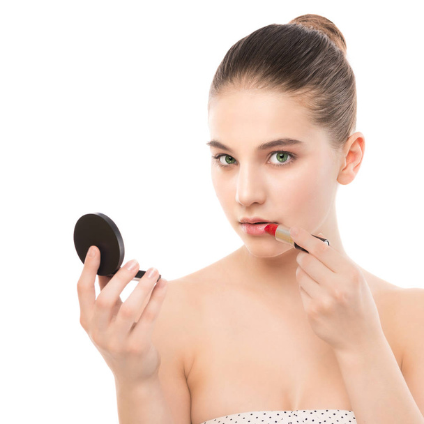 Young brunette woman with perfect clean face applying lipstick using mirror. Isolated on a white. - Foto, afbeelding