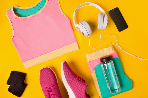 Accesorios de fitness sobre fondo amarillo. Zapatillas, botella de agua, auriculares y top sport
. - Foto, Imagen