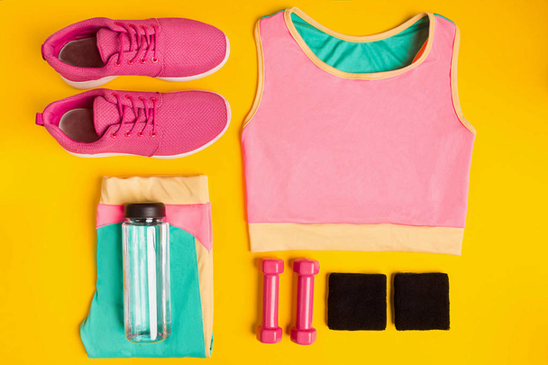 Fitness-Accessoires auf gelbem Hintergrund. Turnschuhe, Wasserflasche, Kurzhanteln und Sporttop. - Foto, Bild