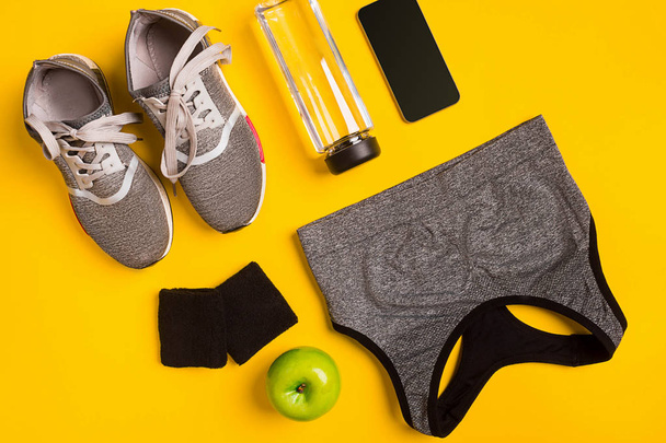 Accessoires de fitness sur fond jaune. Baskets, bouteille d'eau, top smart et sport
. - Photo, image