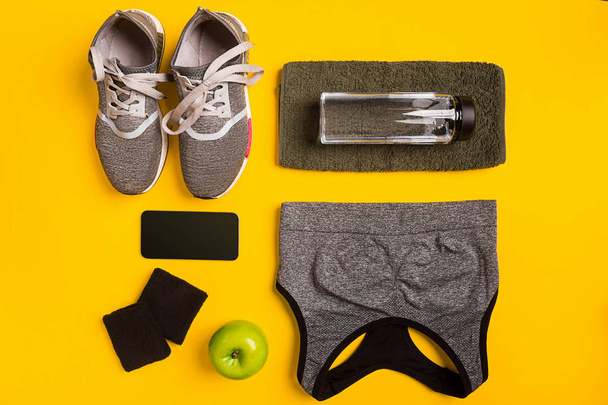 Accessoires de fitness sur fond jaune. Baskets, bouteille d'eau, smart, serviette et haut de sport
. - Photo, image