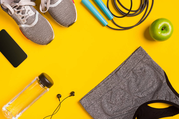 Accesorios de fitness sobre fondo amarillo. Zapatillas, botella de agua, auriculares y top sport
. - Foto, imagen