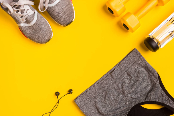 Fitness tartozékok sárga háttéren. Cipők, üveg, víz-, fejhallgató- és sport Top. - Fotó, kép